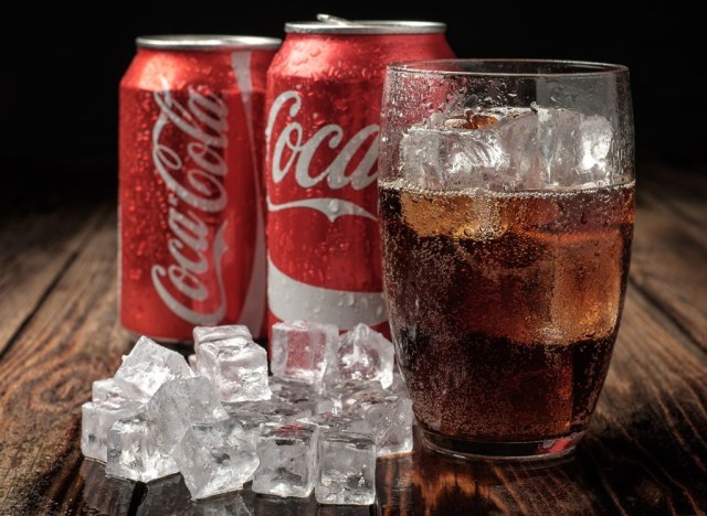Two Coke cans, a glass full of Coke and some ice