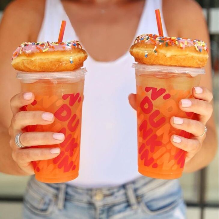Lady holding two Dunkin' Donuts drinks and donuts.