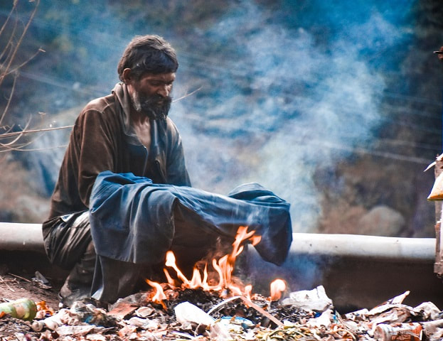 A homeless man sitting next to a fire to keep warm